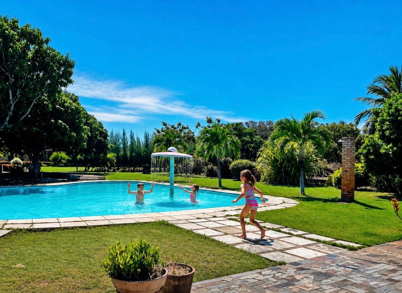 Piscina cercada por jardins tropicais com crianças brincando sob o sol